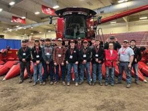 A group of high school age students stand in front of a red combine